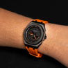 Montre noir et orange porté sur un poignet d'homme sur un fond unie de couleur noir 